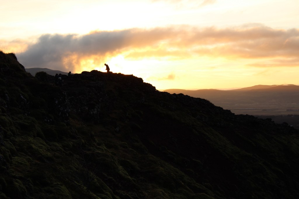 Silhouette of a person in the distance against the sunset on the crater rim.